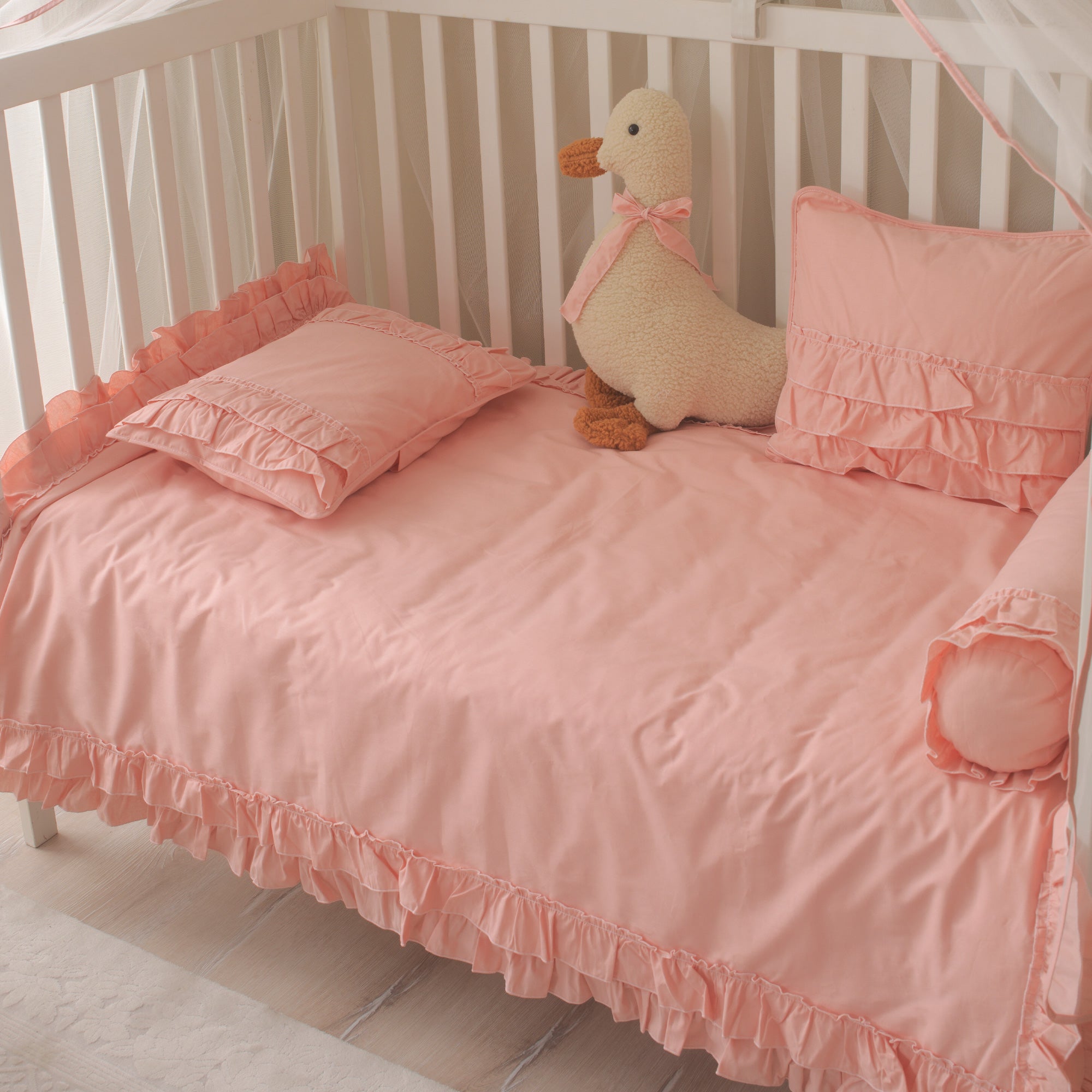 Beşikleri çevreleyen pembe fırfırlı silindir yastık ve güvenli uyku alanı.